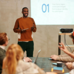 A man delivers a presentation in a modern office to a diverse group of colleagues.
